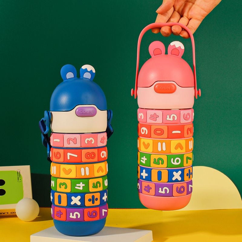Two colorful math-themed water bottles with number blocks are shown against a green backdrop. One bottle is blue and stands on a pedestal, while the other is pink and is being held by a hand.