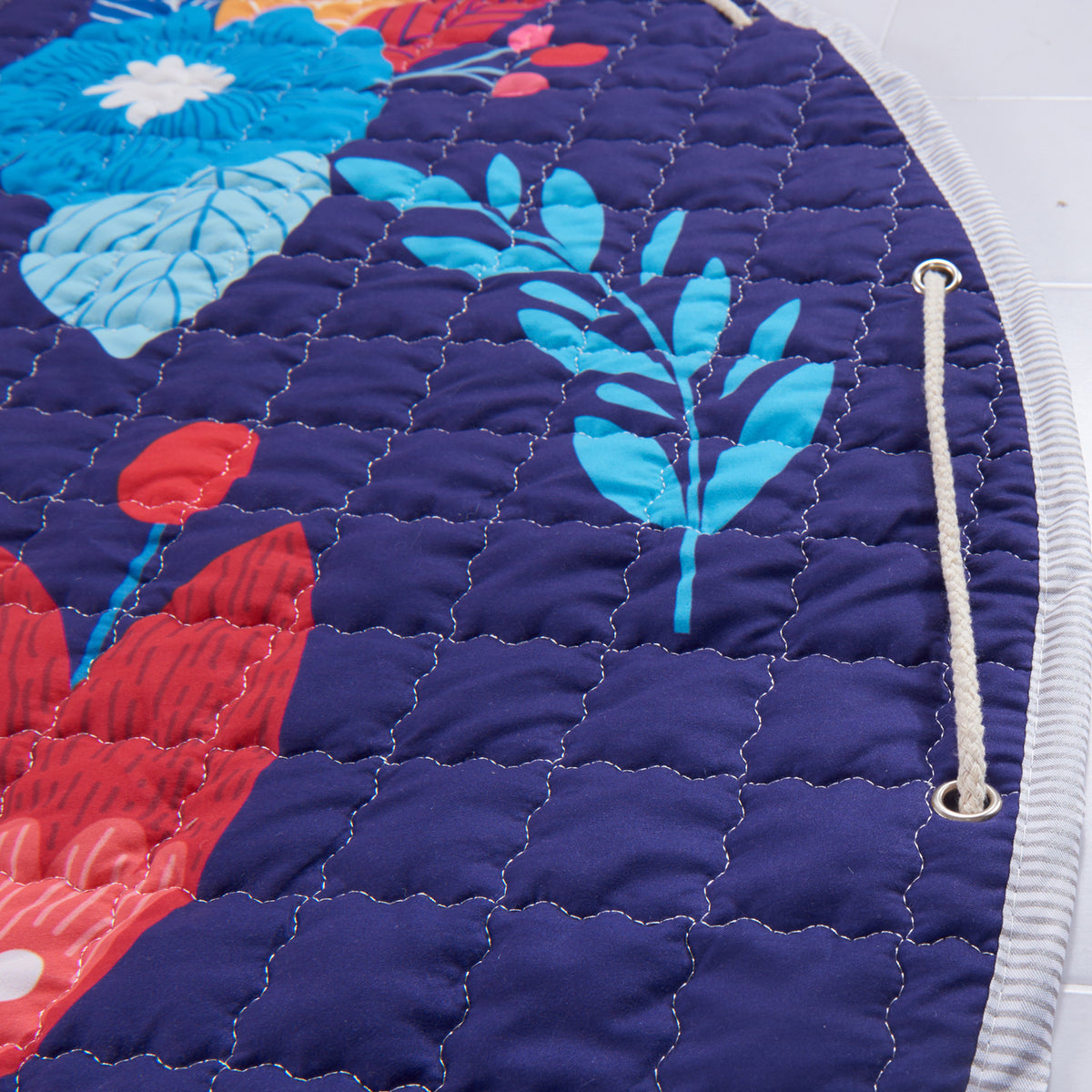 Close-up of a playmat rug with floral patterns on a blue background demonstrating the draw string mechanism