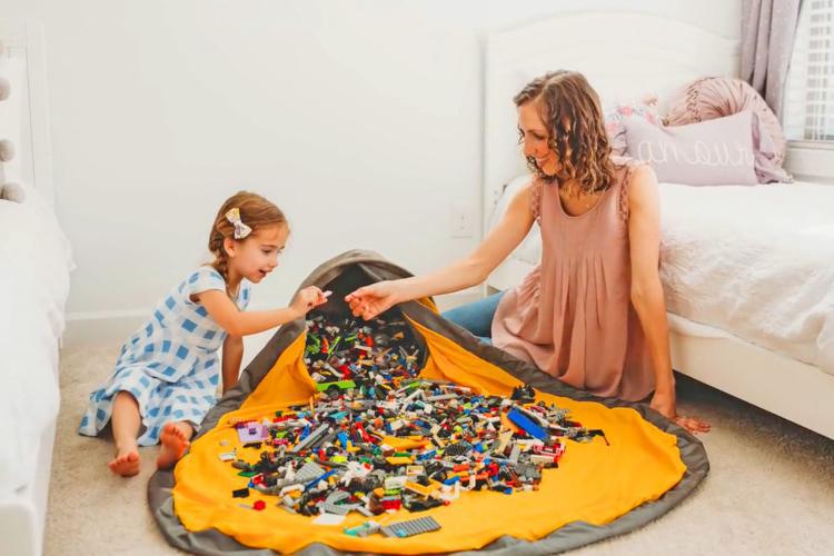 Woman and child playing with toys on a large mat in a bedroom.