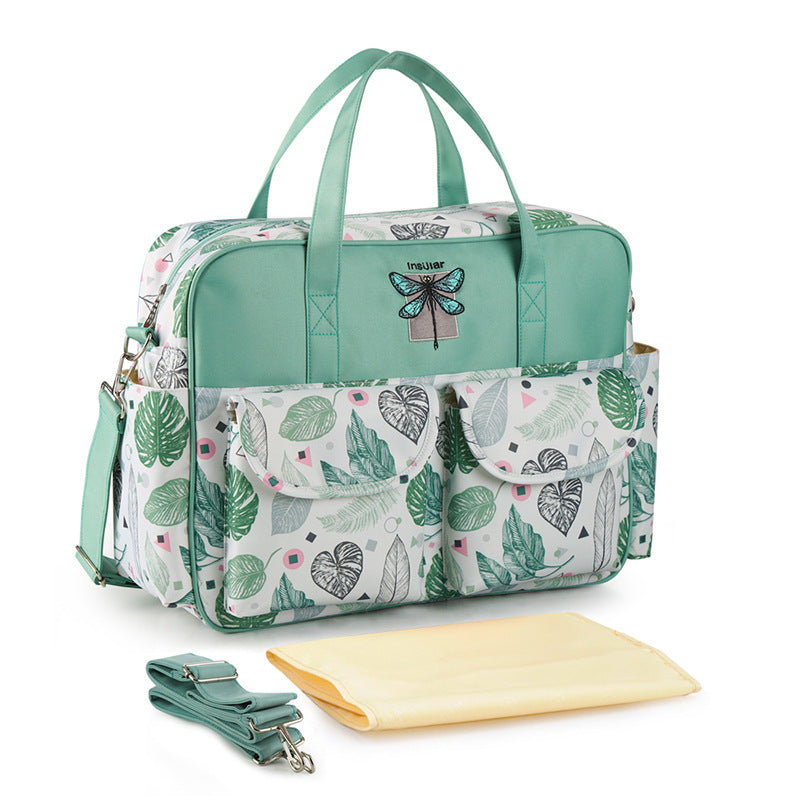 Green diaper bag with leaf pattern and accessories on a white background