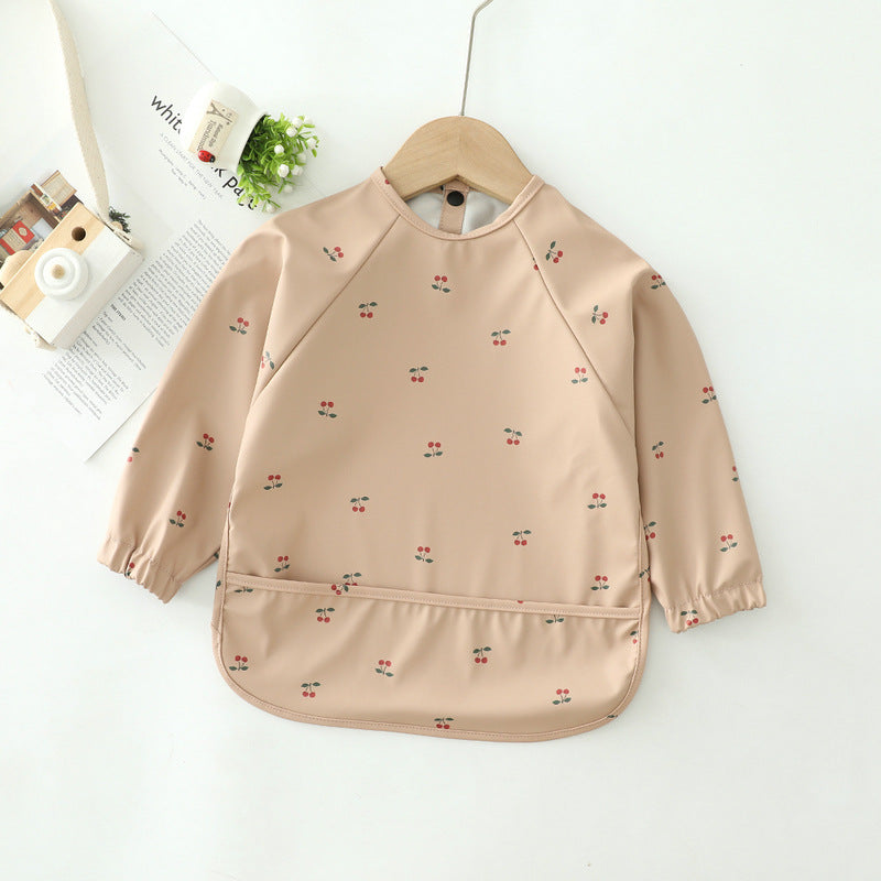 Beige children's bib with cherry pattern on a hanger against a white background