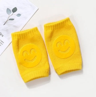 Two yellow elbow pads with smiley face designs on a white background.