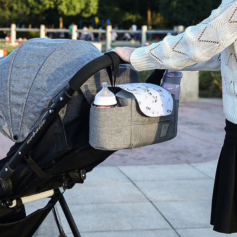 Stroller organizer with bottles and a bag attached to a stroller outdoors.