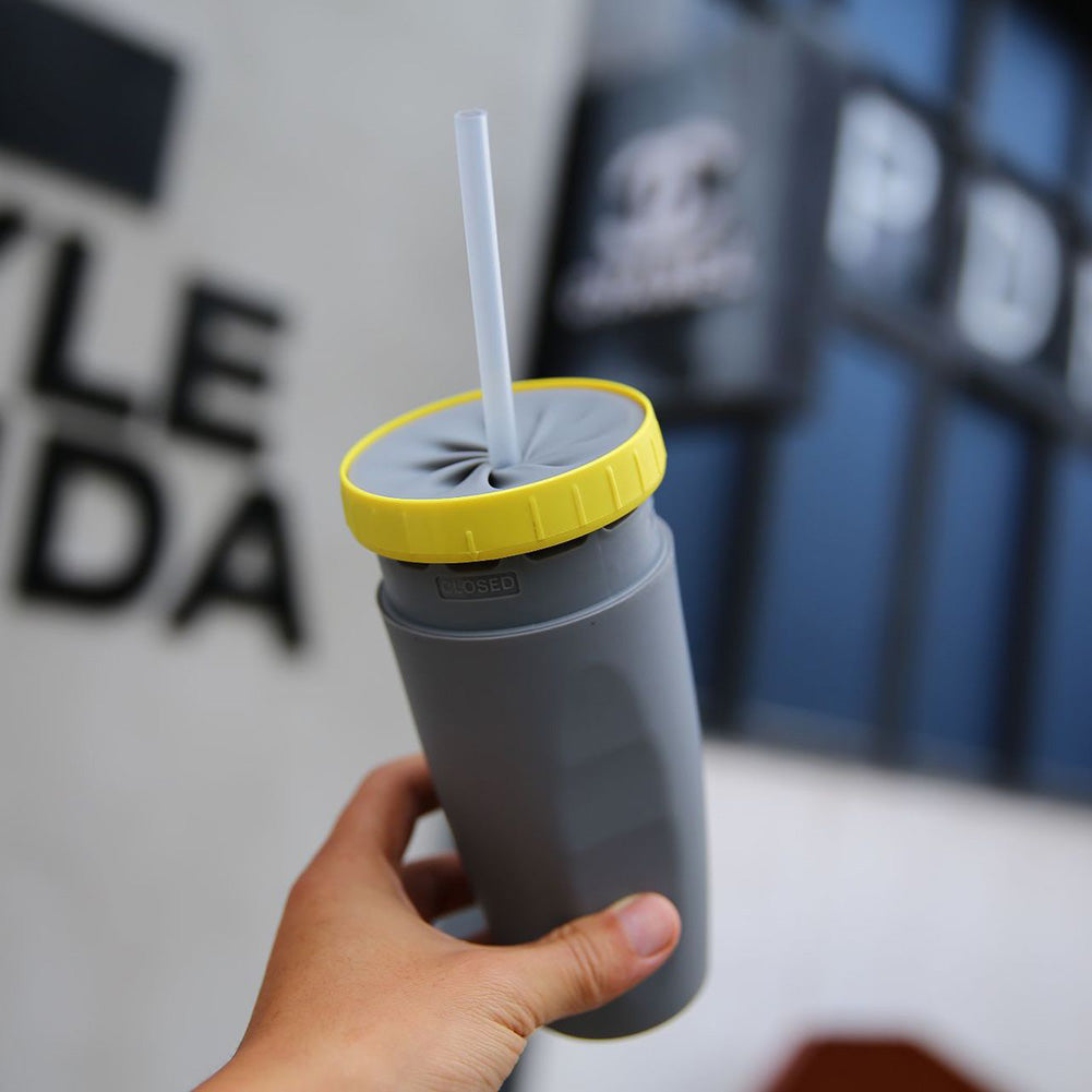 Gray tumbler with yellow lid and straw held by a hand against a blurred background