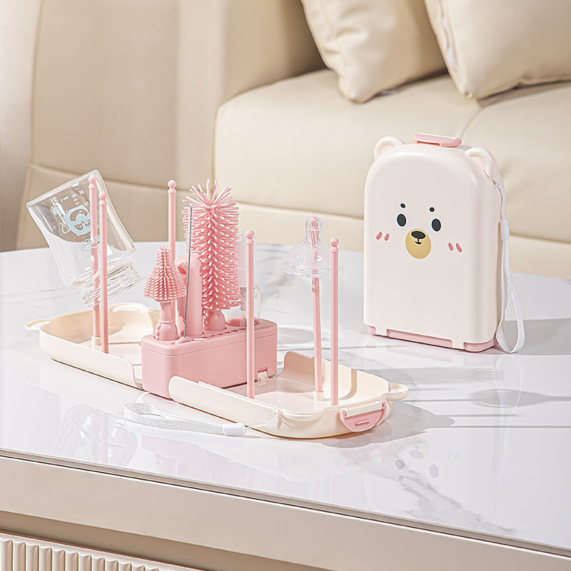 Set of pink baby bottle cleaning utensils and a white appliance with a bear design on a marble surface.