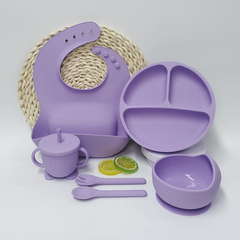 Purple children's dining set including a bib, plate, cup, and utensils on a white background.