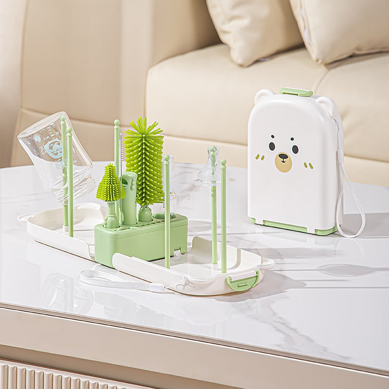 Set of green baby bottle cleaning utensils and a white appliance with a bear design on a marble surface.