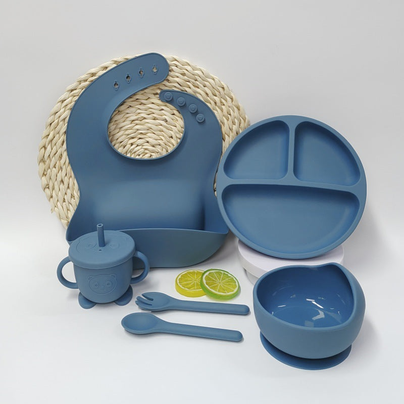 Blue silicone baby feeding set with bib, plate, cup, bowl, and utensils on a white background