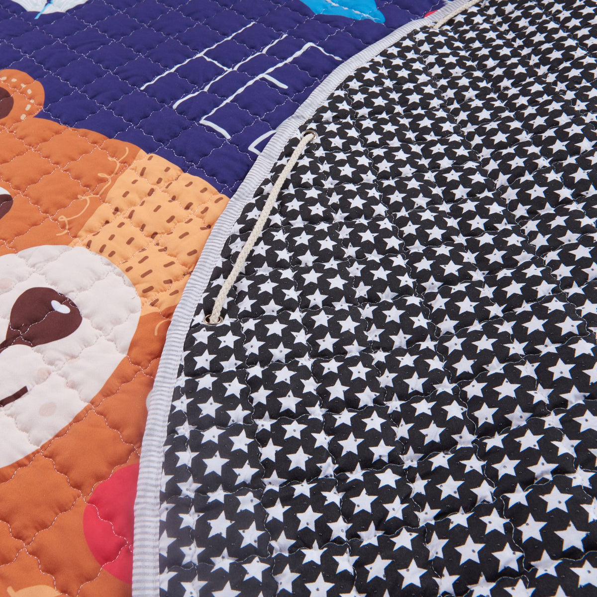 Close-up of a playmat with teddy bear design and star-patterned border demonstrating the draw string mechanism