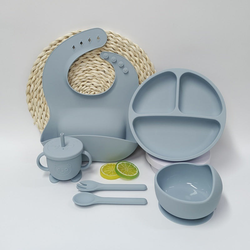 Children's dining set with blue silicone utensils, plate, bowl, and cup on a white background.