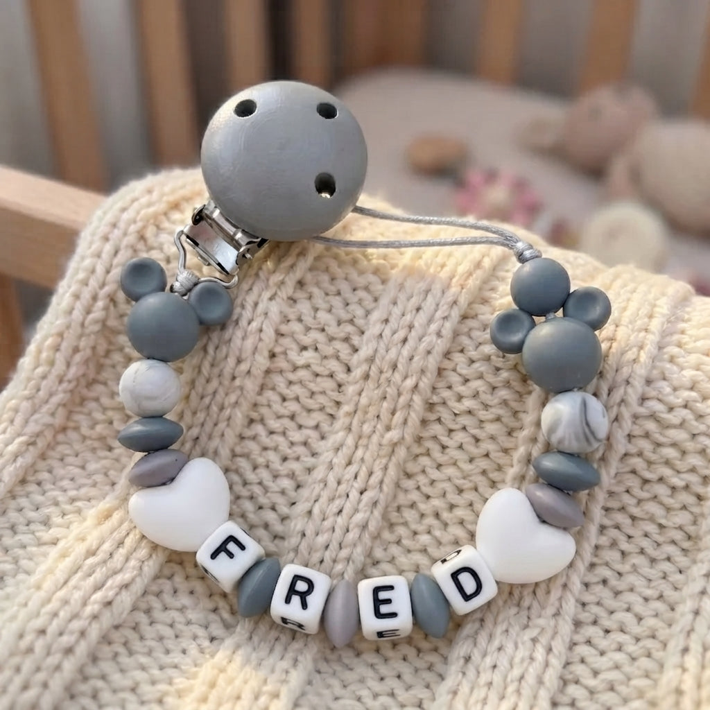A baby pacifier clip made of gray and white silicone beads, featuring a Mickey Mouse-shaped bead, a gray bell, and letter beads spelling 'FRED'.