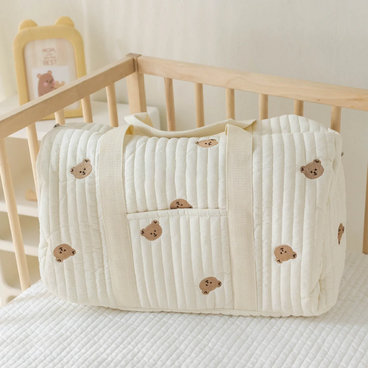Baby crib with a white quilt featuring brown bear illustrations on a neutral background