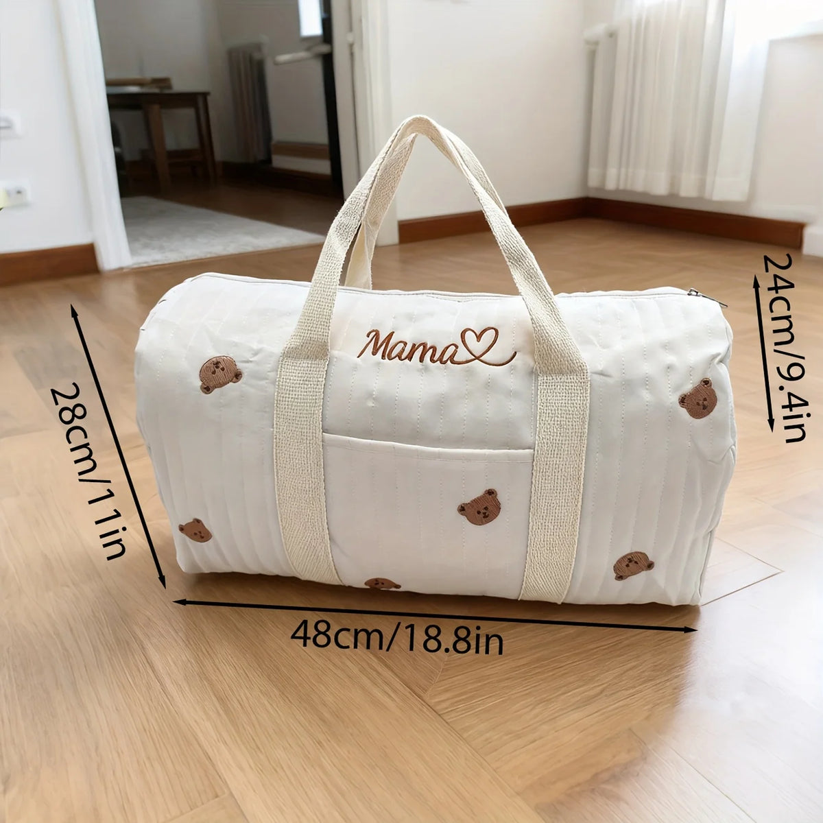 White duffel bag with 'Mama' and bear designs, placed on a wooden floor with dimensions indicated.