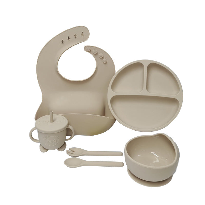 Beige baby feeding set including plate, bowl, cup, bib, and utensils on a white background