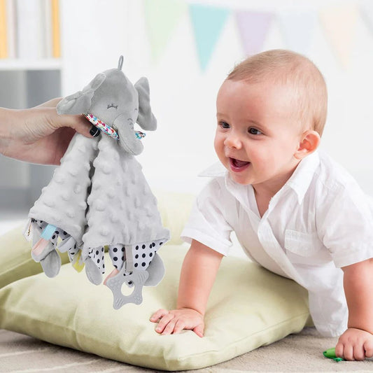 Baby playing with a gray elephant toy on a light green cushion.